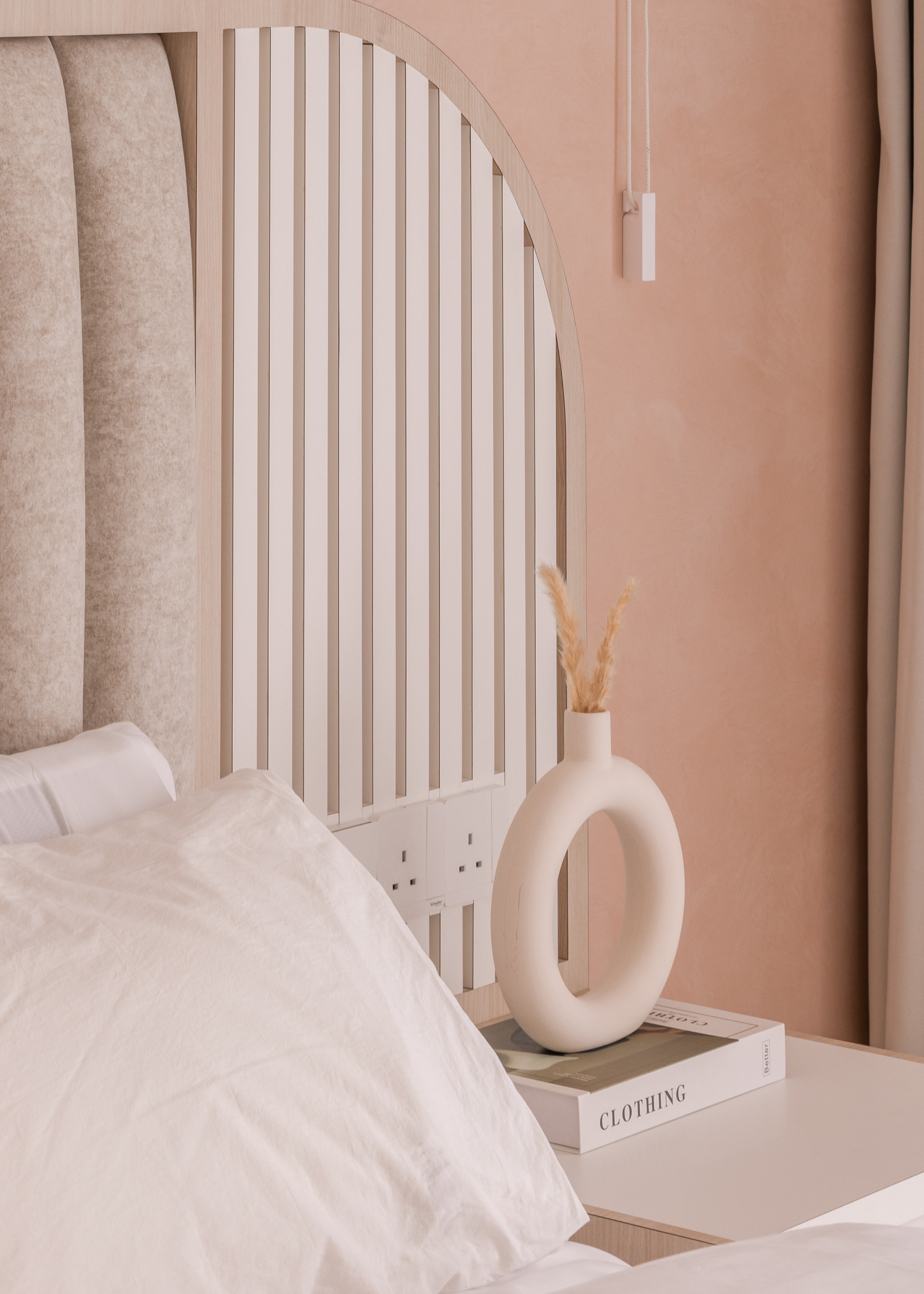 Neatly arranged room with a vase on a nightstand, pillows on a bed, and a neutral color scheme.