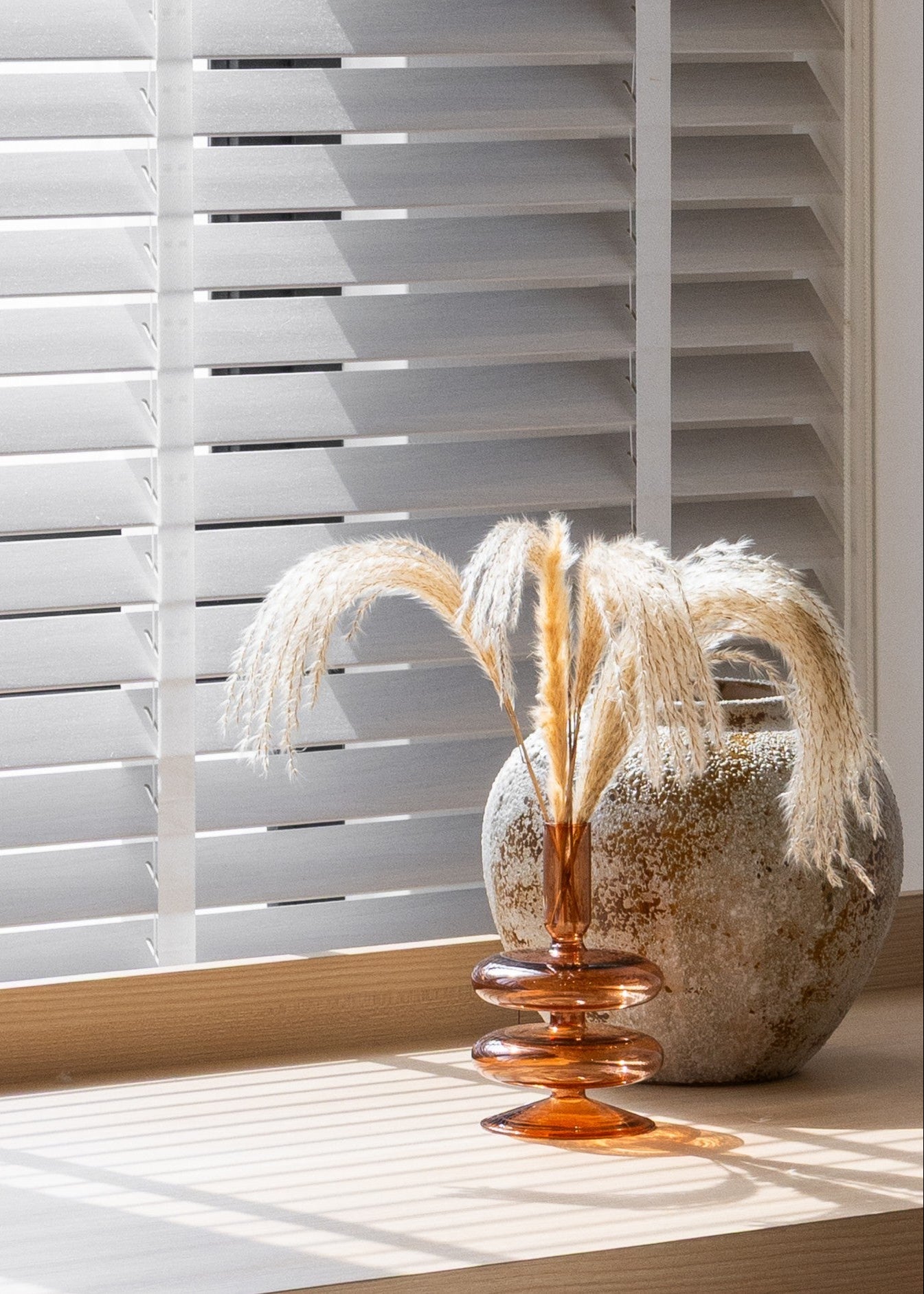 Decorative vase with dried plants on a windowsill with white blinds